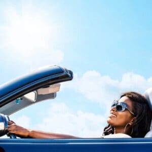 A woman driving in her blue car with the sun shining on it.